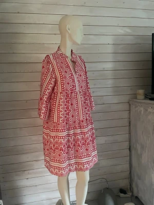 Rödvit mönstrad klänning Emery Rose - Kort klänning från Emery Rose i vitt med rött grafiskt mönster. Klänningen har v-ringning, trekvartsärm och avslappnad passform. Perfekt för dig som gillar boho-vibbar och vill ha något bekvämt men ändå snyggt.