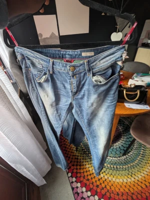 Blå slitna jeans från Traceman/ replay - Säljer ett par blå jeans från Traceman/Replay med slitningar och tvättade detaljer. Klassisk femficksmodell med dragkedja och knapp. Jeansen har en avslappnad passform och är tillverkade i denim. Perfekta för en casual look.