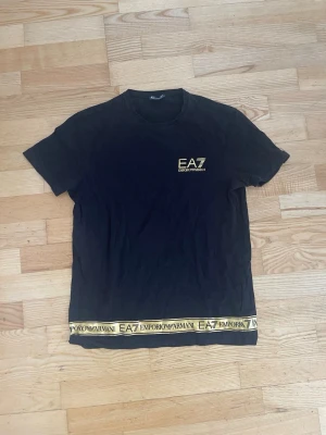 Guld-svart EA7 t shirt  - Svart EA7 Armani t shirt med guldiga detaljer och guldig logga. Väldigt bra skick och är i storlek small. 
