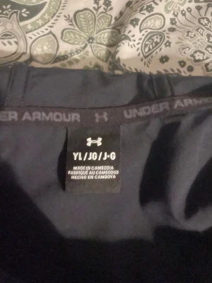 Svart långärmad träningströja Under Armour - Säljer en svart långärmad träningströja från Under Armour. Tröjan har en tight passform och elastisk nederkant med logga runt om. Perfekt för träning eller sportaktiviteter. Materialet är troligtvis syntetiskt för bra andningsförmåga.