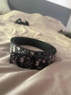 Svart och vit mönstrat bälte - Snyggt bälte i svart och vitt med grafiskt mönster och stilren spänne framtill. Perfekt accessoar för att lyfta din outfit med en modern touch. Bältet har en klassisk form och känns både trendigt och tidlöst.