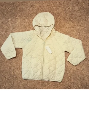 Beige quiltad pufferjacka med huva - Stilren beige pufferjacka med quiltat mönster och dragkedja framtill. Jackan har en praktisk huva och raka ärmar. Perfekt för kalla dagar när du vill hålla värmen och ändå se snygg ut. Materialet är mjukt och lätt vadderat för extra komfort.