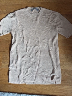 Beige stickad topp från Tiger of Sweden - Snygg beige stickad topp från Tiger of Sweden med rund halsringning och korta ärmar. Tunn och mjuk kvalitet som passar perfekt till många olika stilar. Enkel och stilren design som är lätt att matcha.