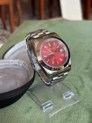 Seiko klocka med röd urtavla - Snygg Seiko herrklocka med rostfritt stålarmband och en iögonfallande röd urtavla med solstrålemönster. Klockan har datumvisning vid klockan tre och tydliga indexmarkeringar.