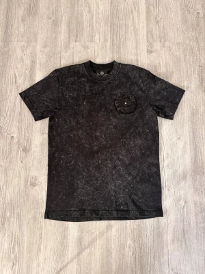 Svart t-shirt från Chrome Hearts - Cool svart t-shirt från Chrome Hearts med stentvättad look. Stor broderad logga på ryggen och mindre broderad detalj på bröstet. Klassisk passform och rund halsringning. Perfekt för dig som gillar streetwear och unika detaljer.