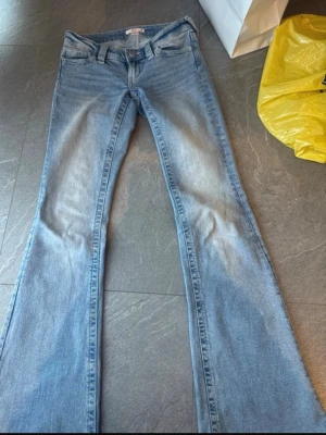 Ljusblå bootcut jeans med brodyr - Säljer ett par ljusblå bootcut jeans med snygg broderad detalj på bakfickorna. Jeansen har klassisk femficksmodell, normal midja och är tillverkade i mjukt denimtyg. Perfekta för dig som gillar retrovibbar och vill ha en avslappnad men trendig look.