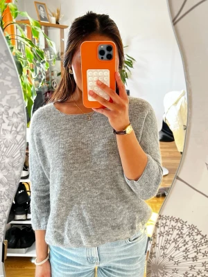 Grå stickad tröja med 3/4-ärm - Mysig grå stickad tröja med rund halsringning och 3/4-långa ärmar. Tröjan har en avslappnad passform och är perfekt att matcha med jeans. Materialet ser ut att vara mjukt och lätt, vilket gör den skön att bära.