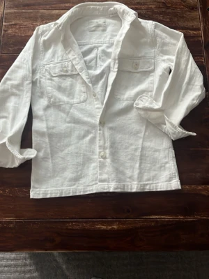 Vit overshirt från Jack & Jones - Klassisk vit skjorta i linne med två bröstfickor och knappar framtill. Skjortan har lång ärm och avslappnad passform, perfekt för en stilren och enkel look. Snygg att bära öppen eller stängd.