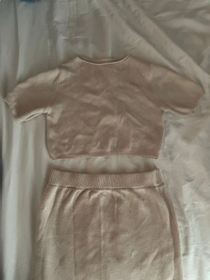 Beige ribbat set med topp och kjol - Säljer ett beige ribbat set med kortärmad crop top och matchande kjol med bred resår i midjan. Setet är i mjukt stickat material och har en enkel, stilren design. Perfekt för dig som gillar minimalistisk och bekväm stil.