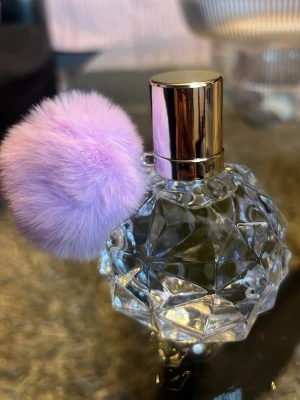 Helt ny! Parfymflaska med lila fluffboll - Säljer en unik parfymflaska i transparent, facetterat glas med guldigt lock och en stor lila fluffboll som dekoration. Flaskan har en modern och lyxig känsla, perfekt som snygg detalj på sminkbordet.