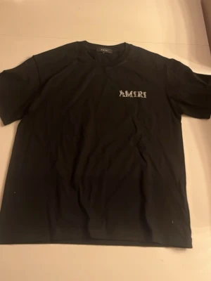 Svart AMIRI t-shirt med tryck Helt oanvänd och pris kan diskuteras  - Svart t-shirt från AMIRI med stort vitt logotryck på ryggen och mindre logga på bröstet. Klassisk passform med rund hals och korta ärmar. Perfekt för dig som gillar streetwear och gillar märke 