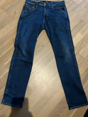  Replay anbass slim fit  - Snygga mörkblå jeans från Replay med klassisk femficksdesign och diskreta slitningar. Jeansen har raka ben och tydliga kontrastsömmar. Perfekta för dig som gillar en stilren och tidlös look. Storlek 32/30