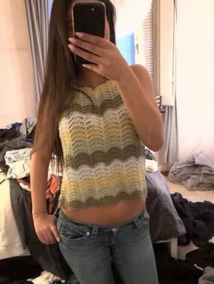 Stickad randig linnetopp i pastell - Säljer en stickad linnetopp med vågiga ränder i ljusgrön, vit och gul. Toppen är ärmlös och har en croppad passform med lätt boho-vibe. Perfekt för varma dagar och enkel att styla med jeans eller kjol.