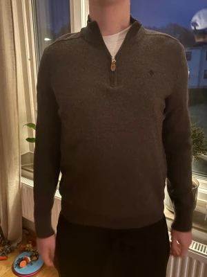 Mörkbrun tröja med halv dragkedja - Mörkbrun långärmad tröja med halv dragkedja och liten broderad logga på bröstet. Tröjan har ståkrage och ribbade muddar. Perfekt för lager-på-lager och snygg till jeans eller chinos. Passar dig som är runt 170