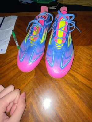 Adidas X Speedportal blå/rosa fotbollsskor - Säljer ett par Adidas X Speedportal fotbollsskor i en riktigt fet färgkombination av blått, rosa och gult. Skorna har snörning, låg profil och är tillverkade i syntetmaterial för lätt vikt och bra bollkontroll. Perfekta för dig som vill sticka ut på planen!