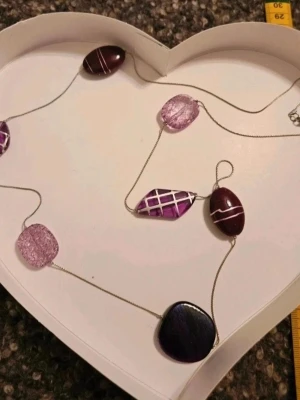 lila halsband - Unikt halsband med stora lila och mörklila glaspärlor/stenar i olika former. Några pärlor har ett rutigt mönster i silver och andra är transparenta med spräcklig effekt. Kedjan är tunn och silverfärgad. Perfekt accessoar för dig som vill sticka ut.  Kan även hämtas I Partille  J