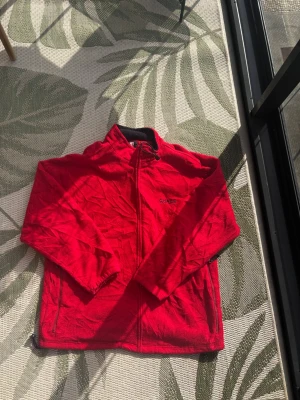 Röd fleecejacka från Chaps Ralph Lauren - Riktigt snygg röd fleecejacka från Chaps Ralph Lauren med dragkedja framtill och broderad logga på bröstet. Jackan har hög krage och är tillverkad i mjukt fleecematerial som håller dig varm under kyliga dagar.