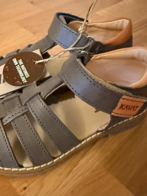 Bruna sandaler från Kavat i läder - helt ny!  - Säljer ett par stilrena bruna sandaler från Kavat med klassisk remdesign och kardborreknäppning. Tillverkade i mjukt läder med beige innersula och kontrastsömmar. Märkeslogga på sidan och vadderad häl för extra komfort.