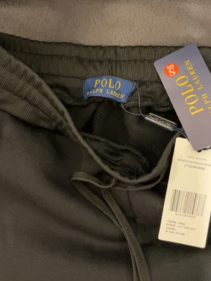 Svarta mjukis set Polo Ralph Lauren - Svarta mjukisbyxor från Polo Ralph Lauren med dragsko i midjan och klassisk vit logga broderad på benet. Tillverkade i mjukt material för maximal komfort och avslappnad passform. Perfekta för chill dagar eller när du vill ha en clean look.