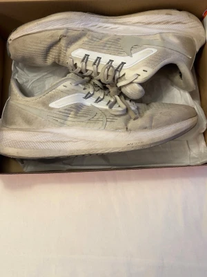 Beige Nike sneakers med vit sula - Snygga sneakers från Nike i beige med vita detaljer och vit sula. Skorna har lågt skaft, snörning och en sportig design med meshmaterial för bra andningsförmåga. Perfekta för dig som gillar en clean och stilren look.