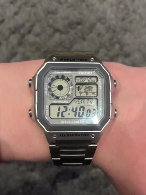 Casio digital klocka i silver - Casio digital klocka med fyrkantig display, världstid, alarm och belysning. Klockan har en robust design i silverfärgat metallarmband och boett. Perfekt för dig som gillar retrostil och funktionella accessoarer.