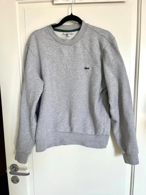 Grå sweatshirt från Lacoste - Säljer en stilren grå sweatshirt från Lacoste köpt på NK. Sparsamt använd. 