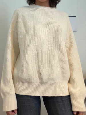 Oversized cremevit stickad tröja - Säljer en oversized stickad tröja i cremevitt med rund hals och breda ribbade muddar vid ärmslut och nederkant. Tröjan har en avslappnad passform och är perfekt för lager-på-lager. Materialet är mjukt och ger en mysig känsla.