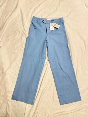 Ljusblå kostymbyxor från Mango - Snygga ljusblå kostymbyxor från Mango med raka ben och klassisk passform. Byxorna har knapp och dragkedja framtill samt är tillverkade i ett stretchigt tyg för extra komfort.