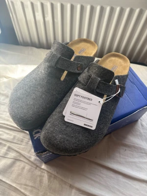  Birkenstock Boston - Säljer ett par Birkenstock tofflor i filtmaterial med justerbart spänne och klassisk korksula. Perfekta för chill dagar hemma eller när du vill ha något bekvämt på fötterna. Stilsäker design och riktigt sköna att gå i. Helt nya och oanvända endast testade inomhus! Hör av er vid eventuella frågor.