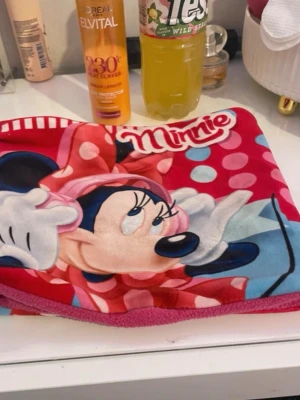 Mjuk fleecefilt med Minnie Mouse - Supermjuk fleecefilt med stort tryck av Minnie Mouse i rött, rosa, blått och vitt. Filten har polkaprickigt mönster och är perfekt att mysa med hemma. Materialet är fleece som känns riktigt gosigt och varmt. Perfekt för dig som älskar Disney och vill ha något färgglatt i sovrummet.