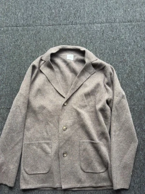 Beige kavaj från John Henric - Stilren beige kavaj från John Henric i mjukt material. Kavajen har två stora framfickor, tre knappar och klassisk krage. Perfekt för en avslappnad men ändå uppklädd look.