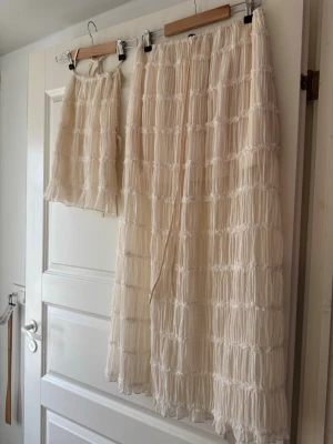 Beige plisserat set med kjol och topp S - Säljer ett superfint tvådelat set i beige med plisserad struktur. Setet består av en lång kjol med resår i midjan och en matchande kort topp. Materialet är lätt och luftigt, perfekt för en trendig look. Inga synliga loggor eller märken.