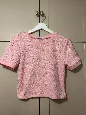 rosa spetsig topp - supersöt ljusrosa croppad topp med korta ärmar och spetsdetaljer. Toppen har ett stickat mönster och rund halsringning, perfekt för en söt och trendig look🩷