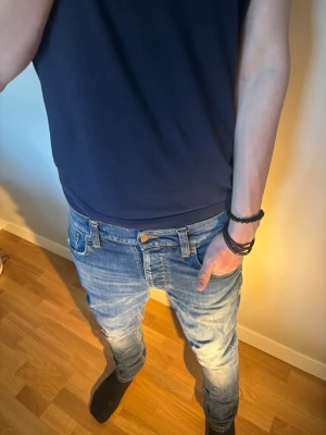 Blå jeans från Nudie Jeans - Säljer ett par snygga blå jeans från Nudie Jeans med klassisk femficksmodell och extremt feta fades. Jeansen har en slim fit passform och är tillverkade i denim med tydliga tvättade effekter. Perfekta för en avslappnad och trendig stil. 
