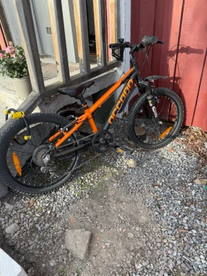 Svart och orange cykel från Accano - Säljer en cool svart och orange mountainbike från Accano. Cykeln har grova däck, växlar och reflexer på hjulen. Perfekt för dig som vill ha en snygg och sportig cykel att cruisa runt på. Ramen är robust och styret är rakt för bra kontroll.