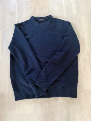 Mörkblå stickad tröja från Indicode - Mörkblå stickad tröja från Indicode med rund halsringning och ribbade muddar vid ärmslut och nederkant. Klassisk och enkel design som passar perfekt till jeans eller chinos. Materialet känns mjukt och bekvämt mot huden. Jag är 176 cm 69kg sitter för stort på mig sitter typ som en L 