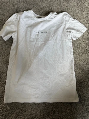 Vit t-shirt Margaux Dietz XS - Vit t-shirt från Margaux Dietz i storlek XS med trycket 'Juan Carlos' på bröstet. Klassisk rund hals och korta ärmar. Tillverkad i mjuk bomull för en skön och enkel stil.