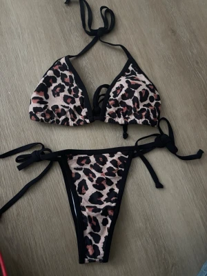 Leopardmönstrad bikini med knyt - Snygg bikini med leopardmönster i beige, svart och bruna toner. Triangeltopp med knyt i nacken och ryggen samt matchande trosa med knyt i sidorna. Perfekt för stranden och solning.Råkade beställa 2 så den är oanvänd😃
