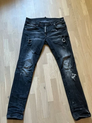 Svarta slitna jeans från Dsquared2 - Säljer ett par svarta jeans från Dsquared2 med skinny fit och slitna detaljer på benen. Jeansen har klassisk femficksdesign, dragkedja och knapp i midjan samt tydliga slitningar och hål för en cool, trendig look.