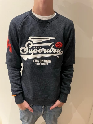 Mörkblå Superdry sweatshirt - Mörkblå sweatshirt från Superdry med stort vitt tryck och japanska tecken på bröstet