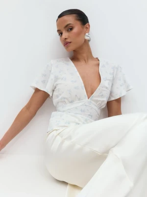 Vit omlottopp med blommigt mönster - Supersöt BNWT helt ny med lappen kvar vit omlottopp från Gina Tricot med ljusblått blommigt mönster. Toppen har korta, vida ärmar, djup v-ringning och knyt i midjan för en smickrande passform. Perfekt för dig som gillar romantiska och feminina detaljer. Storlek S. passar xs-m pga man kan knyta sj. 