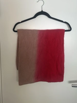 Tvåfärgad mjuk halsduk i rosa och rött - En lång och mysig halsduk i mjuk stickad kvalitet med två färger – ena sidan är dammigt rosa och andra sidan är klar röd. Perfekt för att addera färg till din outfit och hålla dig varm. Halsduken har en enkel, rektangulär form och känns riktigt skön mot huden.