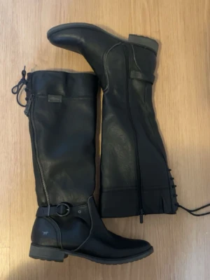 Svarta höga läderstövlar från R - Snygga svarta höga stövlar. Stövlarna har dragkedja på sidan, dekorativ ringdetalj och snörning baktill. Robust sula och klassisk design som passar till många olika stilar. Storlek 40 men små i storlek så passar 39 kanske även 38.