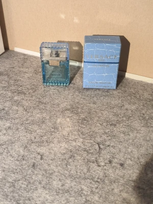 Versace Man Eau Fraîche 5ml - Versace Man Eau Fraîche är en fräsch och modern parfym i en liten, stilren glasflaska med blått mönster och silverdetaljer. Förpackningen är ljusblå med reptilmönster och silvertext. Perfekt för dig som vill ha en exklusiv och trendig doft men vill inte betala ett för stort pris!