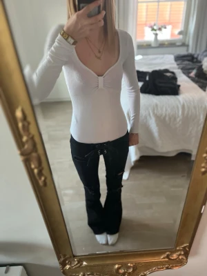Vit body  - Säljer en vit body med lång ärm och djup v-ringning. Toppen har en snygg detalj framtill med rynkning vid bysten och sitter tight mot kroppen. Perfekt att styla med jeans eller kjol för en trendig look.