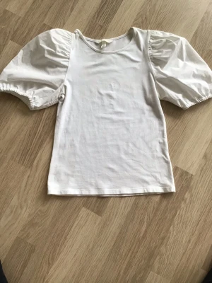 Vit topp med puffärmar från H&M, stl XS - Jättesöt vit topp med stora puffärmar och rund halsringning. Perfekt för dig som vill ha en enkel men ändå statement look. Passar till både jeans och kjol. Storlek XS. Just nu fri frakt, så du betalar bara för toppen. Jag har fler plagg ute, och hittar du något mer från min garderobsutrensning, så skickar jag allt i samma paket.