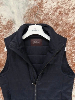 Mörkblå ullväst från Oscar Jacobson - Snygg mörkblå ullväst från Oscar Jacobson med hög krage och dragkedja framtill. Västen har två sidofickor med dragkedja och en stilren, minimalistisk design. Perfekt för lager-på-lager och håller dig varm under kalla dagar. Perfekt till våren. Nyskick 9/10. Nypris 3000 kr. Kvitto ingår. Bara att höra av sig vid frågor // Carl