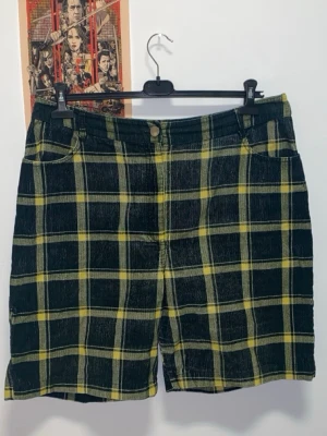 Rutiga ASOS shorts - Snygga shorts med mörkgrönt och gult rutmönster. Manchester material. Bak finns två fickor och ett spänne för extra detalj.