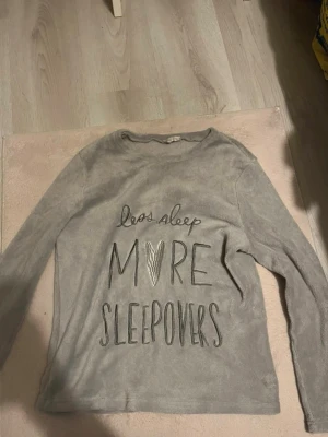 Grå långärmad pyjamastopp - Mysig grå långärmad pyjamastopp i mjukt material med texten 'less sleep MORE SLEEPOVERS' framtill. Perfekt för slappa kvällar och övernattningar. Rund halsringning och avslappnad passform.