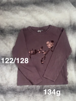 Lila långärmad topp med paljetter - Lila långärmad topp med glittrande paljettdetaljer i form av en gren och ett hjärta på bröstet. Rund halsringning. Perfekt för dig som gillar lite extra bling i vardagen.